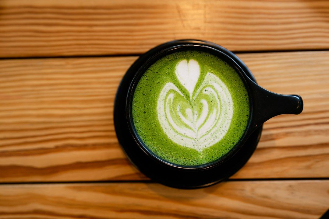 Taza negra con matcha latte verde brillante decorado con latte art en forma de corazón sobre mesa de madera