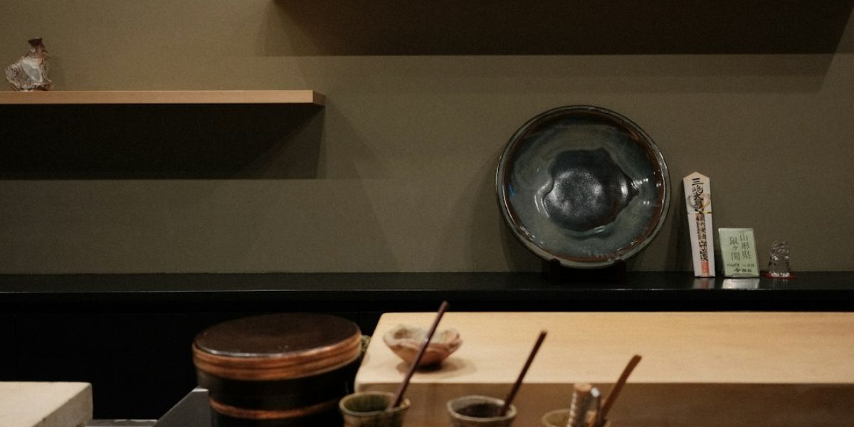 Mostrador de madera con cuencos de cerámica negra, recipientes con líquidos y varillas de bambú para preparar té matcha