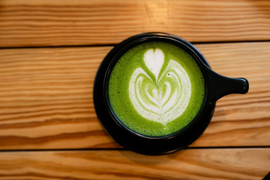 Taza negra con matcha latte verde brillante decorado con latte art en forma de corazón sobre mesa de madera