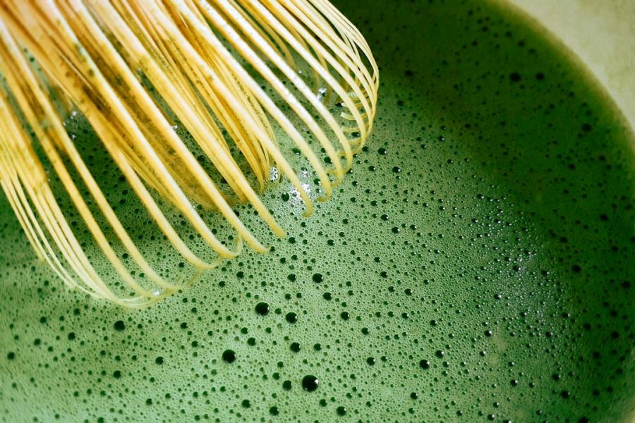 Batidor de bambú tradicional en contacto con matcha verde con espuma y burbujas características de la bebida