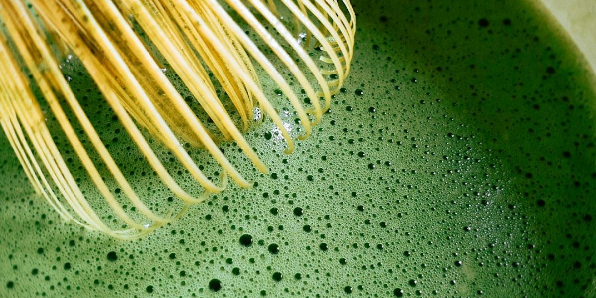 Batidor de bambú natural sobre té matcha verde espumoso con burbujas, mostrando la preparación tradicional