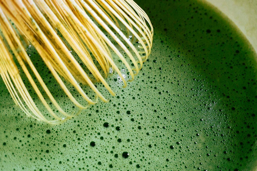 Batidor de bambú natural sobre té matcha verde espumoso con burbujas, mostrando la preparación tradicional