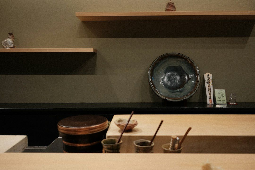Mostrador de madera con cuencos de cerámica negra, recipientes con líquidos y varillas de bambú para preparar té matcha