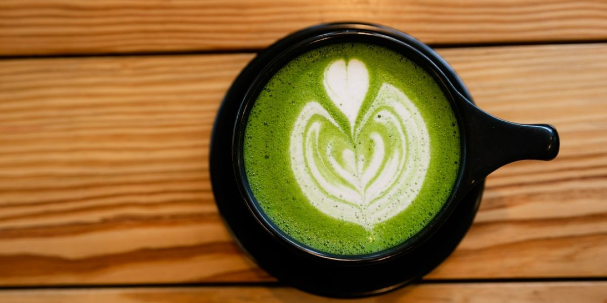 Taza negra con matcha latte verde brillante decorado con latte art en forma de corazón sobre mesa de madera